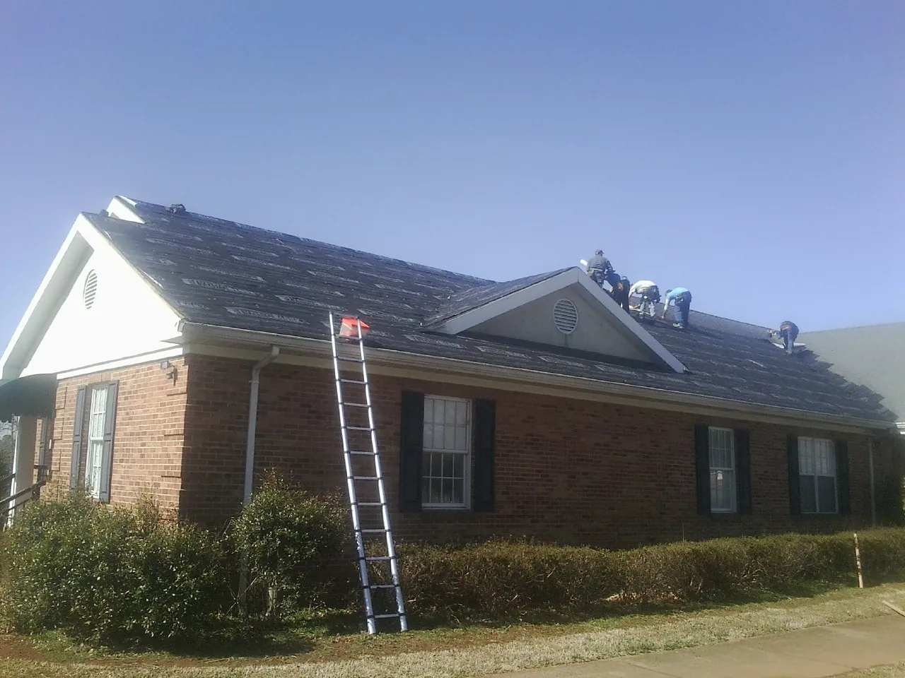 Crew tearing shingles off a brick ranch roof with a ladder set — Metal Roof Repair work by our crew in North Bridgton