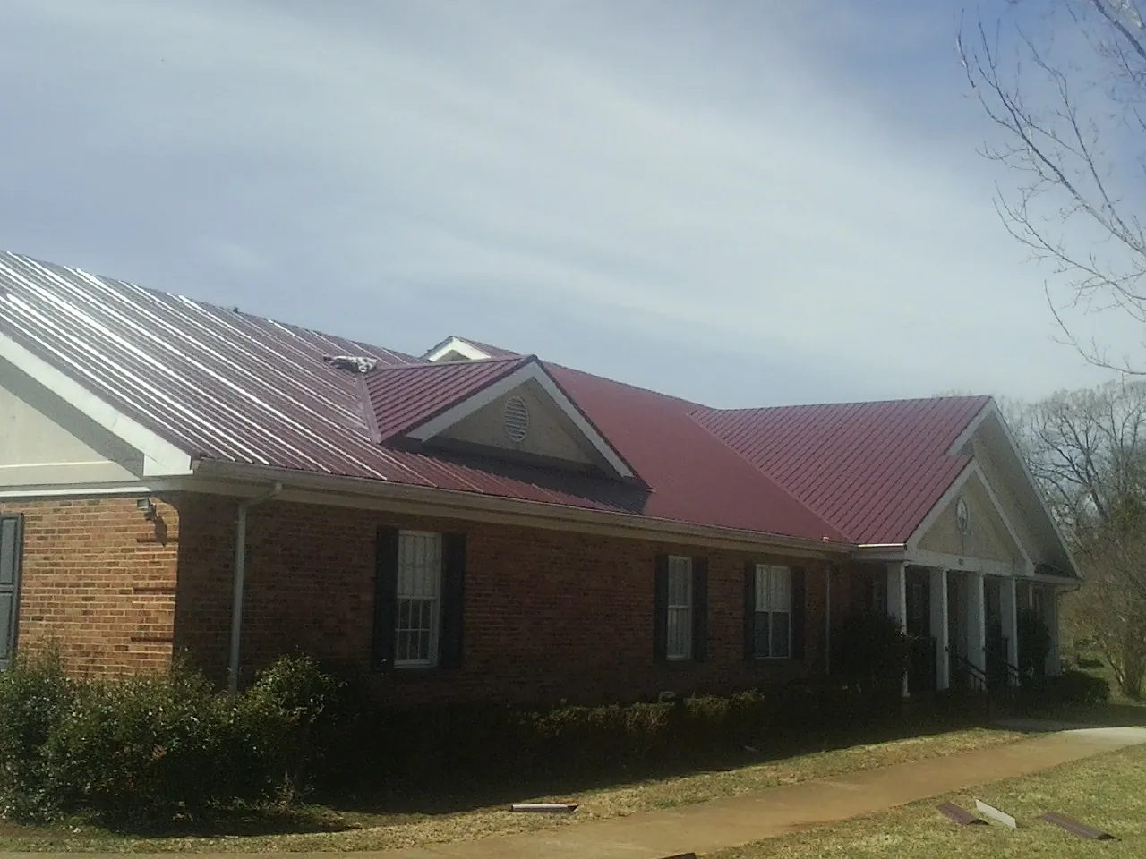 Red metal roof with gabled entries on a long brick building, from a Hail Damage Roof Repair job in North Bridgton