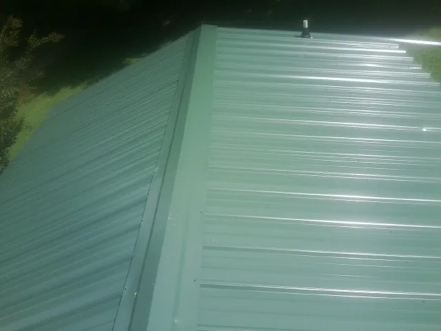 New green metal panels meeting at the ridge of a roof — Flat Roof Repair work by our crew in North Bridgton