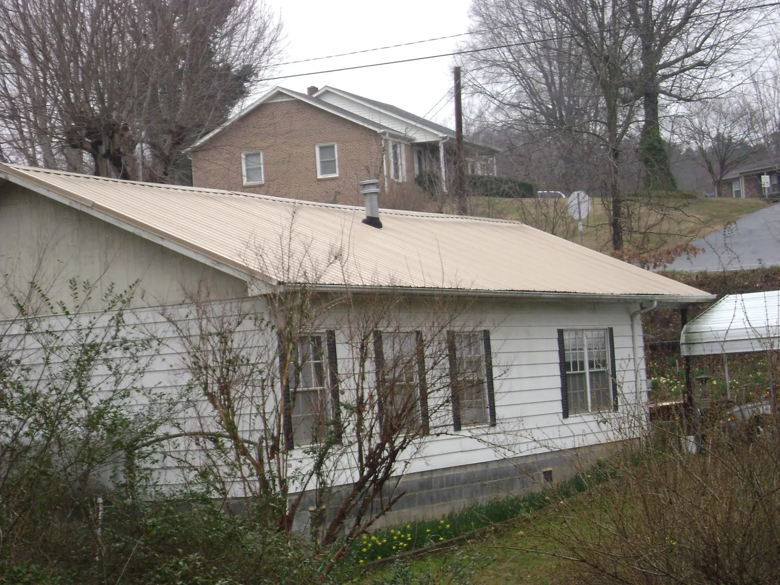 Tan metal roof on a white sided house set into a hillside — Commercial Roofing by Roofing Brothers in North Bridgton