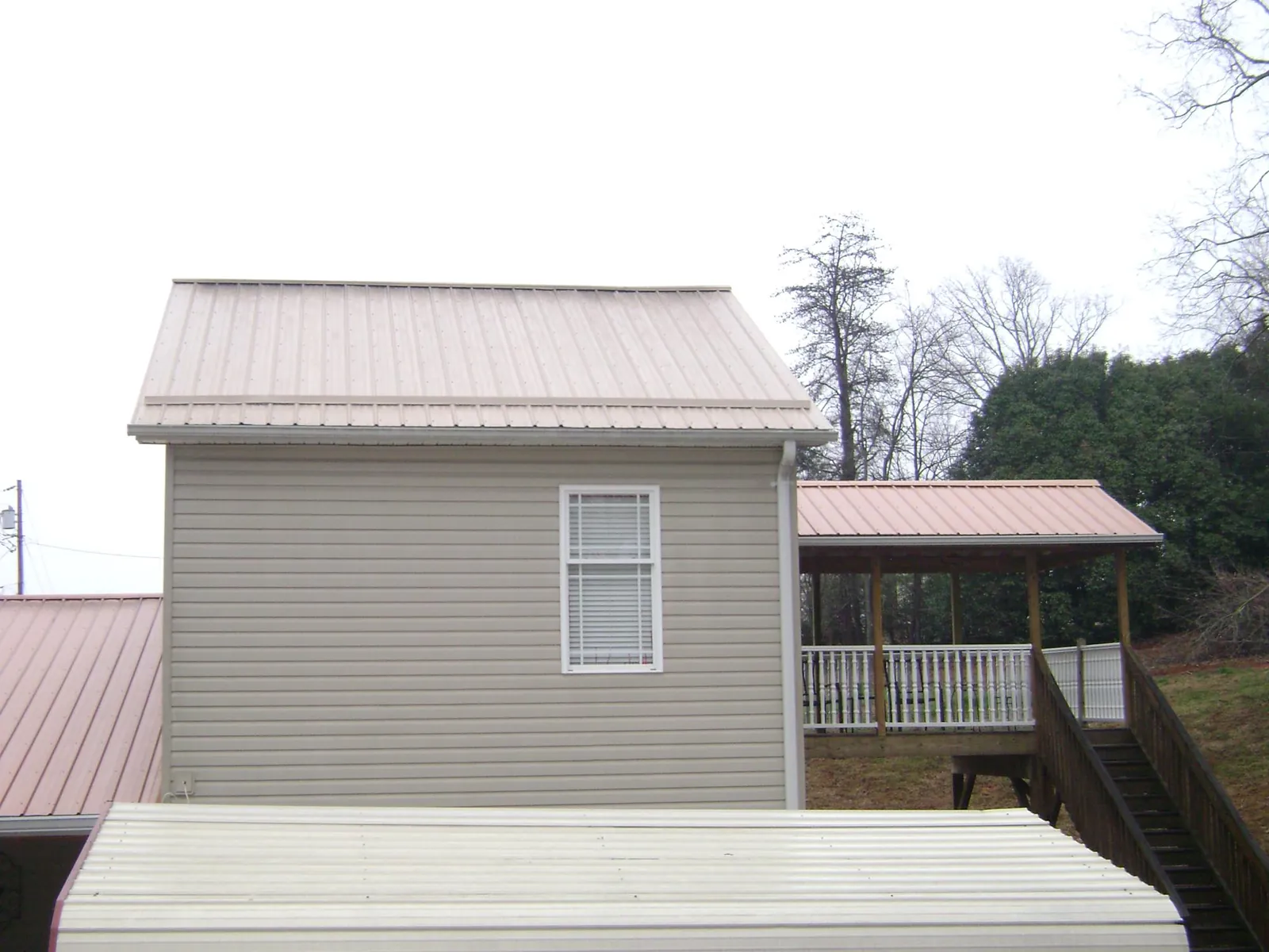 Tan metal roofs on a two story addition and attached porch, from a Roof Replacement job in North Bridgton
